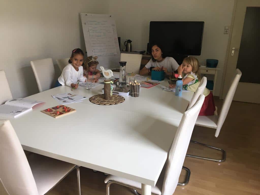 Drei Kinder und Lehrerin sitzen an einem Tisch und lernen